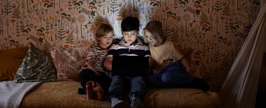 Tre barn tittar på dator i säng.