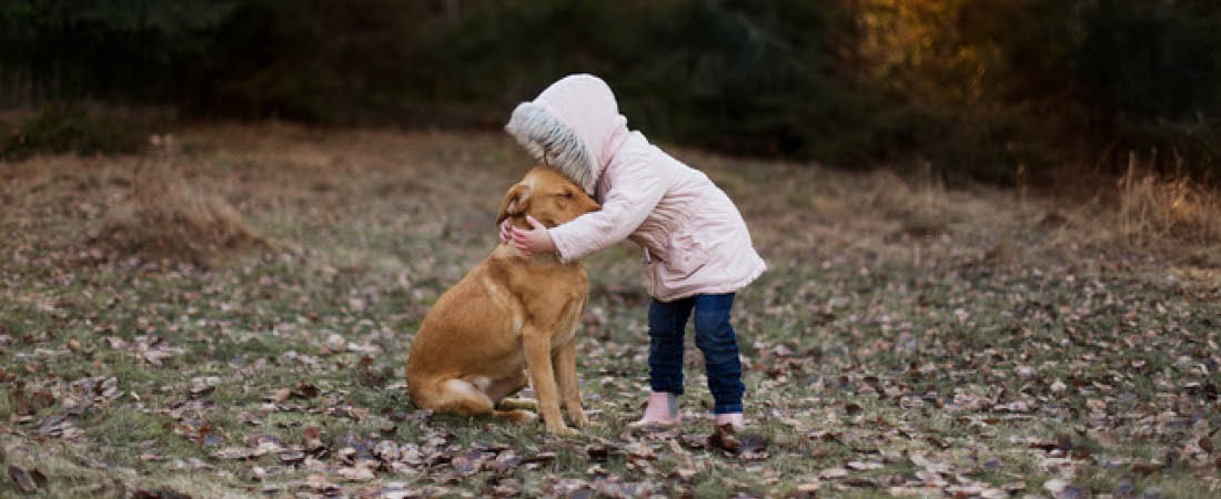 En flicka i rosa vinterjacka kramar sin hund i skogen.