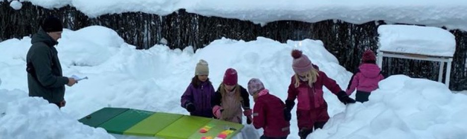 Barn utomhus i vinterlandskap. Dom leker vid ett bord som är gjort av snö.