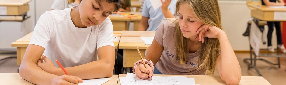 Två barn sitter vid ett skrivbord i skolan. Dom gör läxor.