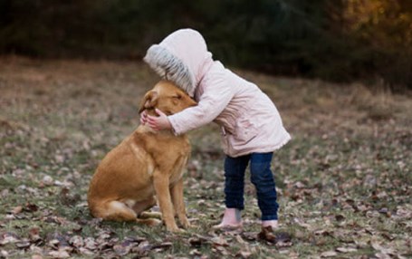 Ett barn i rosa jacka kramar sin hund.