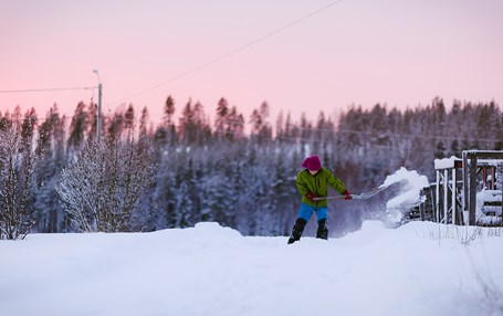 Pojke gräver i snö. Rosa himmel och mycket snö i bakgrunden. 