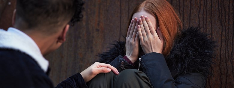 Pojke tröstar flicka som gråter. Flickan täcker ansiktet med händerna.