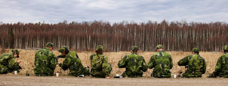 Militärer sitter på en rad vid en vägkant och fikar.