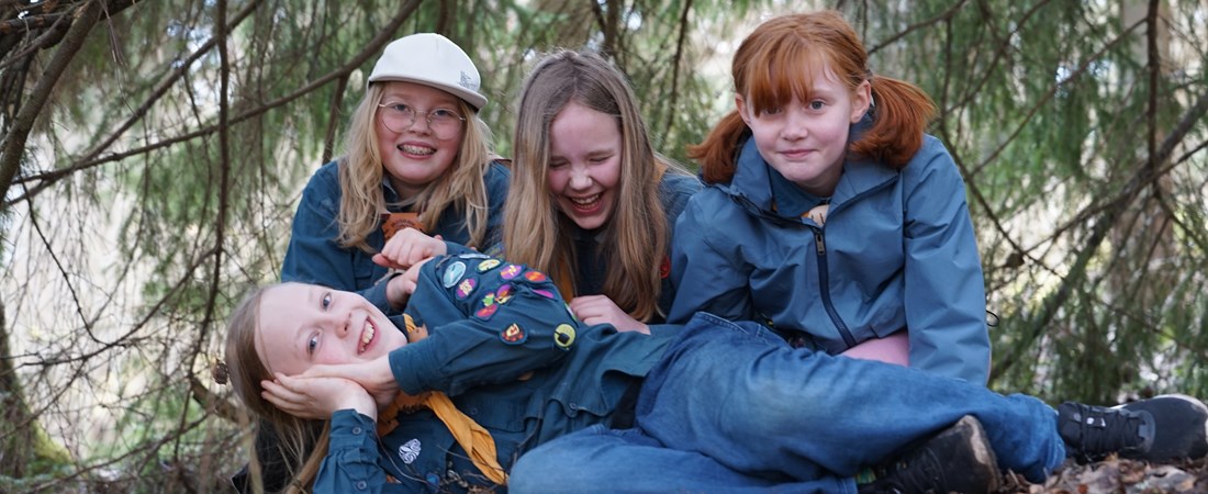 Fyra barn i scoutskjortor under en gran. 
