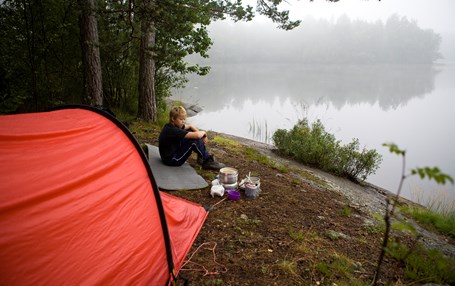 Barn sitter på en klippa vid en sjö. I bakgrunden står ett tält. Bredvid barnet finns ett stormkök uppställt. 