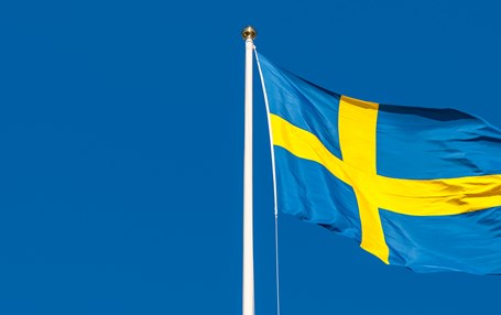 Svenska flaggan vajar i vinden mot blå himmel.